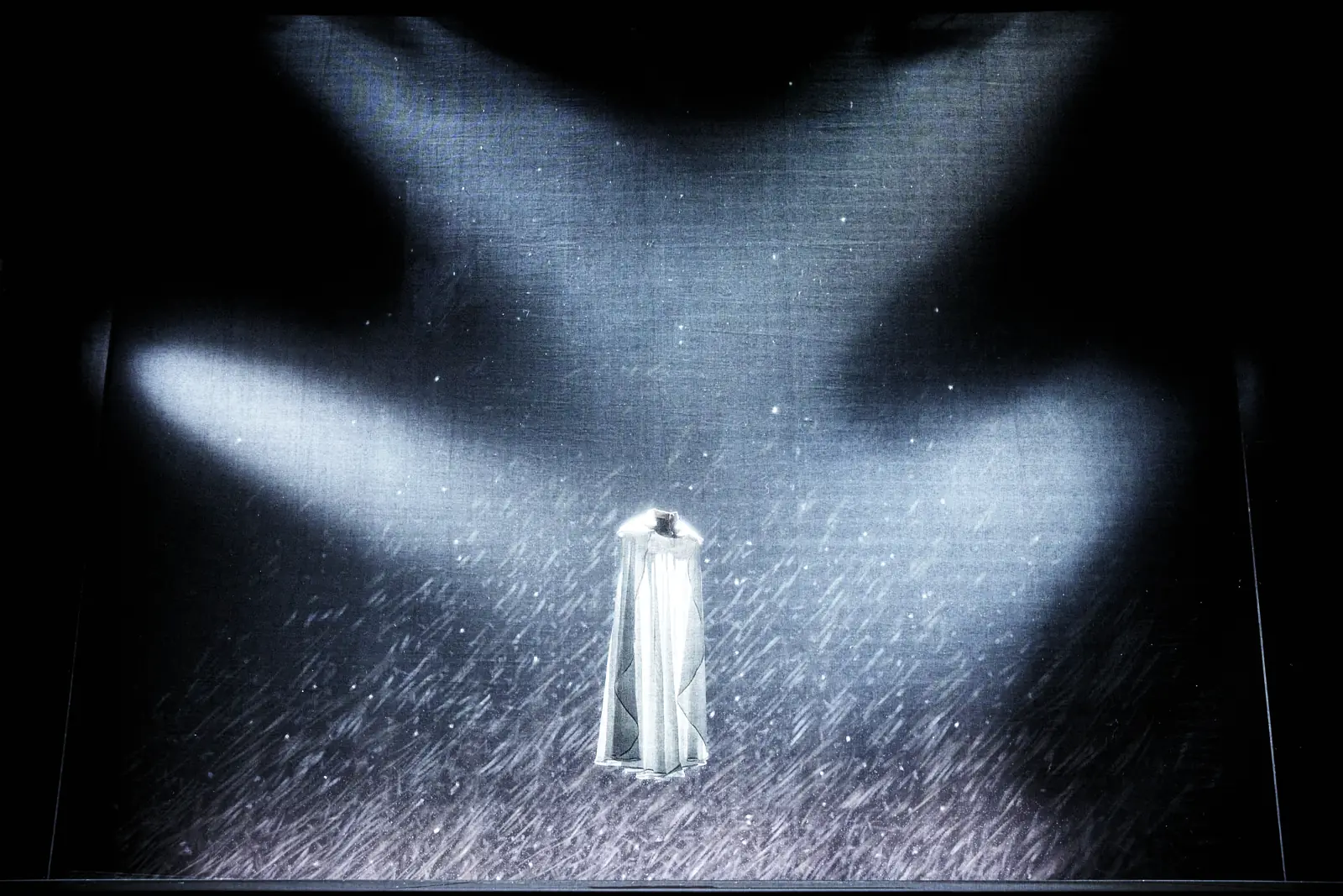 Apparition d'une silhouette blanche dans un faisceau de lumière et une pluie de particules, sur un plateau de théâtre