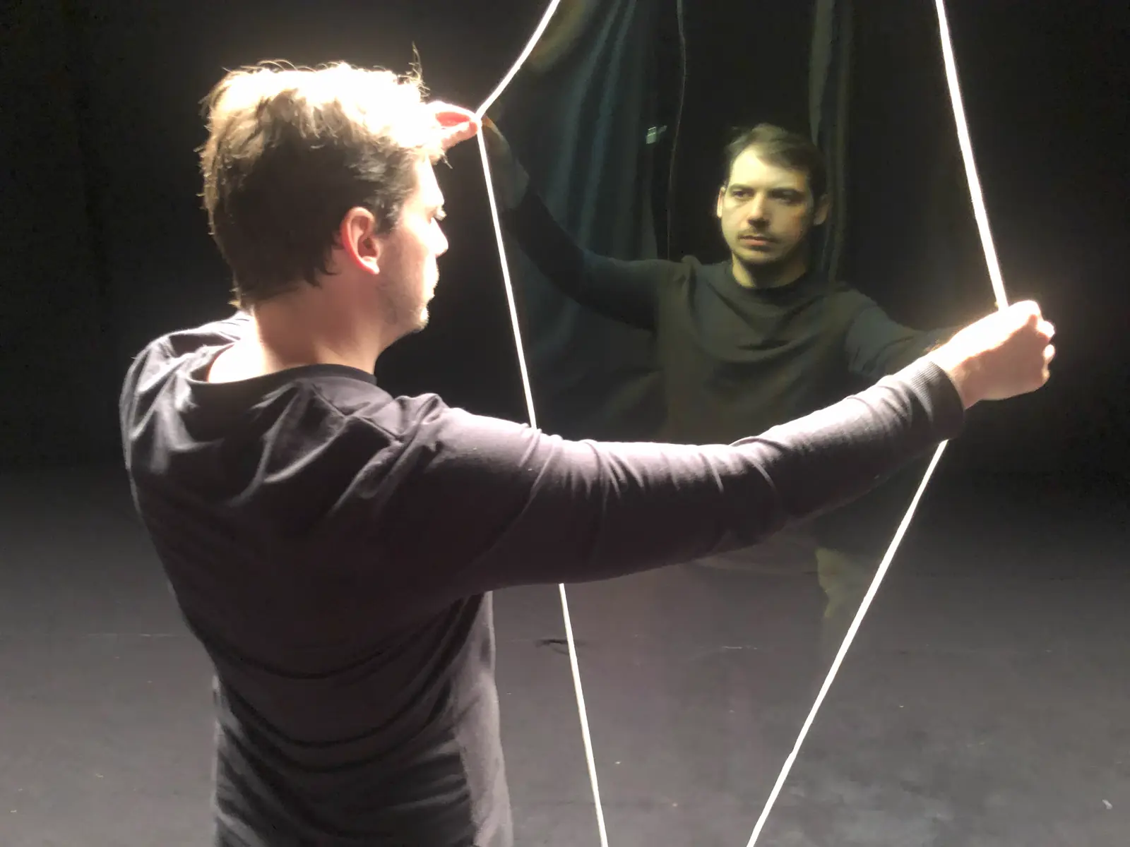 Deux techniciens tendent des fils d'illusion sur un plateau de théâtre pendant une répétition